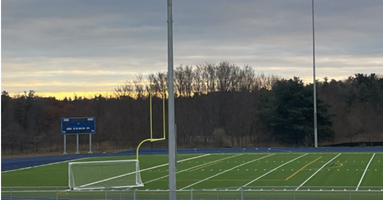 Turf field with score board , football field goal posts and soccer nets, trees in the background