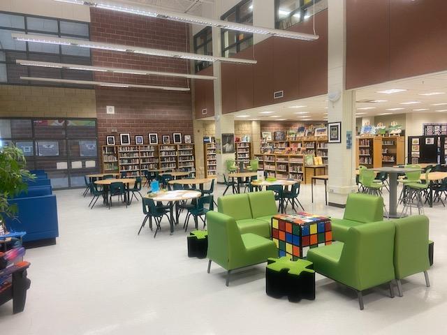 view of the library, shelves of books in the backgrounds, tables with seating in the foreground