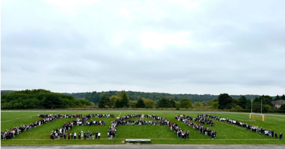 Green sports field shown, with students standing together spelling out the word team